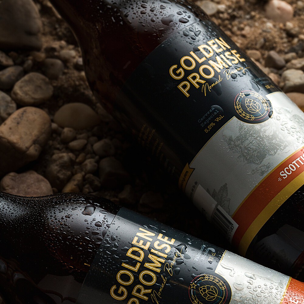 Dos botellas de la cerveza Golden Promise sobre tierra y piedras